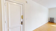 This single-floor residence offers two bedrooms and one bathroom within a efficiently arranged layout. Throughout the living areas and bedrooms, warm-toned hardwood floors add character and a sense of continuity. The entry area features crisp white walls and clean white trim, with a classic paneled door fitted with brass hardware that sets a timeless tone from the moment you step inside.

The spacious primary bedroom is notably generous, filled with natural light streaming through multiple windows dressed with horizontal blinds. A cast-iron radiator provides classic charm while offering reliable in-unit heating. A ceiling fan with lighting anchors the room, and two white panel doors — one leading to a closet and another to the hallway — add functional convenience.

The second bedroom is similarly bright, with windows on two walls inviting ample daylight and a ceiling fan overhead, along with its own radiator for comfort.

The bathroom retains vintage character with classic white hexagonal tile flooring, white subway-tiled walls, a pedestal sink, and a wall-mounted sconce beside a framed mirror. A window with blinds provides natural light and ventilation, completing the clean, timeless aesthetic of this well-preserved space.