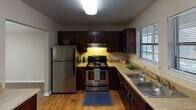 Located at 1175 Pineville Rd in Chattanooga, Tennessee, this single-floor residence offers a thoughtfully designed layout with a blend of hardwood-style flooring and plush carpeting throughout. The kitchen is a standout feature, equipped with rich dark cabinetry, stainless steel appliances including a refrigerator and range, a double sink, and a pass-through counter that connects seamlessly to the dining and living areas. Natural light filters in through a window above the sink, adding warmth to the space.

The open living and dining area is generously proportioned, with soft carpeting, a textured ceiling, and a central pendant light fixture. Large sliding glass doors and French doors lead to an outdoor balcony, filling the space with natural light and providing outdoor access. The bedrooms are well-sized, each featuring carpeted floors, neutral walls, and windows with blinds. The primary bedroom includes access to a walk-in closet area.

Two bathrooms serve the residence, each finished with dark wood vanities, light countertops, and hardwood-style flooring. A dedicated laundry room with built-in wire shelving and a washer hookup adds everyday convenience, rounding out this functional and comfortable Chattanooga home.