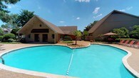 Located at 711 Harbour Dr in Ridgeland, Mississippi, this single-story property offers a welcoming and well-appointed environment designed for comfort and outdoor enjoyment. The standout feature of the property is its generously sized outdoor swimming pool, which takes center stage in the exterior space. The pool's vivid turquoise water is complemented by clean tile edging and a classic lane divider, conveying a sense of resort-style leisure.

Surrounding the pool is a spacious concrete deck that provides ample room for lounging and outdoor activities. Lush, mature trees frame the perimeter of the property, offering natural shade and a sense of privacy. Decorative landscaping elements, including manicured shrubs and a distinctive palm tree near the pool's edge, add a tropical touch to the setting.

The building itself features a pitched, brown shingled roofline that extends over a covered patio area, complete with pendant lighting and a decorative star accent — lending the space a charming, rustic character. A gated enclosure adds an additional layer of security and definition to the outdoor area. The overall ambiance is bright, open, and inviting, making this property a distinctive offering in the Ridgeland community.