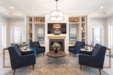Located at 129 NC-801 S in Bermuda Run, NC, this thoughtfully designed single-floor space offers a well-appointed open layout connecting the kitchen, dining, and living areas, complemented by two hallways that guide circulation throughout. The herringbone-patterned parquet flooring is a defining architectural detail, lending warmth and visual interest across the entire floor.

The kitchen is a standout feature, anchored by a large waterfall-edge marble island with seating for multiple guests, navy-blue cabinetry, stainless steel appliances, and a textured tile backsplash. An industrial-style geometric chandelier overhead adds a contemporary finishing touch. The adjacent dining area flows naturally from the kitchen, creating a cohesive entertaining space.

The living room is centered around a shiplap fireplace flanked by built-in shelving on both sides, providing both storage and display space. A circular chandelier and coordinating navy accent chairs contribute to the room's polished, cohesive aesthetic. Large windows throughout the space allow ample natural light to fill the interior, enhancing its bright and welcoming ambiance. The overall design balances modern sophistication with comfortable, functional livability.