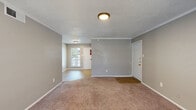 This single-floor residence offers a practical and well-organized layout designed for comfortable everyday living. The living area is generously sized, finished with plush wall-to-wall carpeting and neutral gray walls that create a calm, cohesive atmosphere throughout. A large window allows natural light to fill the space, offering a bright and welcoming feel. Crown molding and textured ceilings add a layer of architectural detail, while a flush-mount ceiling light provides consistent overhead illumination. The entryway transitions seamlessly from the living area and features durable wood-look flooring that extends into the kitchen. The galley-style kitchen is efficiently designed with gray cabinetry, granite-look countertops, a double-basin sink, and black appliances including a refrigerator and electric range, maximizing functionality within a compact footprint. The bedroom is a well-proportioned, carpeted retreat with neutral tones and a window that lets in natural light. Both bathrooms are identically appointed with wood-look flooring, granite-look vanity countertops, and full tub-shower combinations with tiled surrounds, offering clean and functional spaces. Overall, the unit presents a consistent and understated aesthetic with practical finishes throughout.