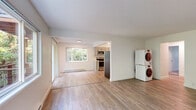Located in Beaverton, Oregon, this 2-bedroom, 1-bathroom single-floor home offers a clean, updated interior with a practical and comfortable layout. Light wood-style flooring runs throughout the main living areas, complementing the bright, neutral palette of white and soft gray tones. The open living room is generously sized, filled with natural light from a large picture window that frames views of mature surrounding trees, and is served by baseboard heating. A sliding glass door leads to a covered balcony where wood-beam detailing and a wire-panel railing overlook a lush, green canopy—a tranquil outdoor retreat. The kitchen has been thoughtfully renovated with gray shaker-style cabinetry, white countertops, a teal subway tile backsplash, stainless steel appliances including a range, microwave, dishwasher, and refrigerator, and light wood flooring. Both bedrooms feature plush carpet, ceiling fans, and windows with wooded views; the primary bedroom includes a mirrored sliding closet. Three closets provide ample storage throughout. The full bathroom is bright and clean, featuring a tub-shower combination and wood-style flooring. A stacked washer and dryer unit is conveniently located within the home, adding everyday practicality to this move-in-ready residence.