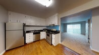 Located at 13475 Bancroft Ave in San Leandro, CA, this single-floor unit offers a functional and well-organized layout designed for comfortable everyday living. The kitchen serves as a central feature, equipped with stainless steel appliances including a refrigerator, electric range, dishwasher, and microwave. White cabinetry extending to the ceiling provides generous storage, while dark granite-style countertops offer a clean contrast. Hardwood flooring runs throughout the kitchen, which opens through a pass-through counter toward the living area. The living space is carpeted and receives natural light through a large sliding glass door fitted with vertical blinds, creating a bright and open atmosphere. Additional carpeted rooms serve as bedrooms, each featuring vertical blind-covered windows and ceiling fans for comfort and ventilation. One bedroom also includes a wall-mounted air conditioning unit for supplemental climate control. The bathroom is finished with light tile flooring, a combination tub and shower, white cabinetry with open shelving, and a window for natural light. Throughout the unit, neutral gray wall tones and clean white trim contribute to a cohesive, understated aesthetic.