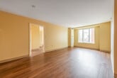 This well-appointed single-floor residence offers a cohesive and functional layout designed for comfortable urban living. Throughout the space, rich hardwood flooring in a warm walnut tone creates a polished, continuous flow between rooms, complemented by clean white baseboards and soft cream-colored walls that lend a bright, welcoming atmosphere.

The open living area is generously proportioned, with large windows that frame views of the surrounding urban streetscape, allowing natural light to fill the room throughout the day. The space provides ample room for flexible furniture arrangements and benefits from a clean, uncluttered design aesthetic.

The bedroom is a well-sized private retreat, featuring the same hardwood flooring and warm wall tones, with a door providing separation from the main living area. The room offers a calm and quiet setting suited for rest.

The kitchen is efficiently laid out with white cabinetry, dark granite-style countertops, and tile flooring, with a pass-through opening that connects it to the main living space. A hallway leads from the kitchen area to the front entry door, providing a clear and practical circulation path.

The bathroom is finished with light ceramic tile flooring, a white vanity with under-sink storage, a medicine cabinet mirror, and consistent warm-toned walls, offering a clean and functional space.