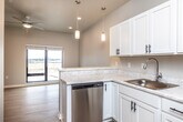 This single-floor unit offers a clean, modern design with an open-concept layout that seamlessly connects the kitchen and living area. The kitchen is a standout feature, equipped with crisp white shaker-style cabinetry, black hardware accents, light stone-look countertops, and a full suite of stainless steel appliances including a refrigerator, electric range, over-the-range microwave, and dishwasher. Pendant lighting hangs above the kitchen peninsula, adding a contemporary touch while enhancing the sense of openness. Light wood-tone flooring runs throughout the unit, contributing to a bright and cohesive aesthetic. The living area benefits from natural light streaming through a large window, and a ceiling fan provides year-round comfort. The bedroom is generously proportioned, featuring a sliding glass door that frames views of the surrounding landscape, along with a ceiling fan and ample wall space. The bathroom is efficiently designed with a walk-in shower, a white vanity with an integrated sink, and consistent light flooring that ties the space together. A textured ceiling in the main living area and recessed lighting throughout add depth and practicality. The overall ambiance is fresh, clean, and move-in ready, reflecting a thoughtfully designed contemporary living space.