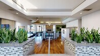 Located at 1801 Eureka Rd in Roseville, CA, this expansive single-floor community living space offers a thoughtfully designed, open-plan layout that seamlessly connects multiple functional zones. Rich hardwood flooring flows throughout, anchoring the contemporary aesthetic and reflecting the abundant natural light that pours in through floor-to-ceiling windows along the exterior walls.

The space is organized into distinct yet interconnected areas. A central lounge features a large sectional sofa, accent chairs in bold green upholstery, and a statement globe chandelier suspended beneath a coffered ceiling with a skylight above. Adjacent to this is a dedicated entertainment zone with a billiards table, ottomans, and wall-mounted televisions, bordered by dramatic curved walls and soaring ceilings with a tray detail.

A quieter sitting area offers a blue sectional sofa, marble-topped coffee table, and built-in TV niche framed by a gracefully curved wall. Decorative wall sconces, mosaic-tiled planter dividers housing tall indoor plants, and a stone-accented fireplace add texture and warmth throughout. A dining area with a green accent wall, pendant lighting, and high-top seating provides additional utility.

The overall ambiance is modern, sophisticated, and inviting, making this a well-appointed communal gathering space.