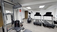 Located at 236 W Walnut Lane in the Germantown neighborhood of Philadelphia, PA, this fitness facility offers a dedicated workout environment designed to support a range of exercise routines. The space is thoughtfully laid out on a single floor, maximizing usability and accessibility for users of all fitness levels.

The workout area is equipped with a variety of exercise machines, including treadmills, an elliptical trainer, and a multi-function cable strength training machine, providing options for both cardiovascular and resistance training. The flooring is a durable, neutral-toned surface well-suited for a high-traffic fitness environment.

Natural light filters in through skylights embedded in the drop ceiling, brightening the space and creating an open, energizing atmosphere. A wall-mounted split air conditioning unit ensures year-round climate comfort during workouts. The walls are finished in a clean white, contributing to the bright and functional ambiance of the room. A private door at the rear of the space provides additional access or utility. Safety and informational signage is posted near the equipment, reflecting a well-maintained and responsibly managed facility. Overall, this fitness space offers a practical and efficient environment for regular exercise.