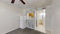 Located at 1402 Fannidella Dr in Carrollton, TX, this single-floor, one-bedroom, one-bathroom unit offers a functional and straightforward layout. The main living area is finished with gray carpet and features a ceiling fan overhead, contributing to a practical, comfortable environment. A front entry door with a sidelight window allows natural light to filter into the space, brightening the carpeted interior.

The kitchenette area is defined by a decorative stone-textured accent wall surrounding a pass-through counter with overhead wood-toned cabinetry. A full-size refrigerator fits neatly alongside the counter, maximizing the utility of the compact kitchen space. The transition from the carpeted living area to tile flooring marks the boundary between the main room and the kitchen and bathroom zones.

The bedroom is generously proportioned relative to the overall footprint of the unit, providing ample room for standard furnishings. White walls throughout maintain a clean, neutral aesthetic.

The bathroom is fully equipped with a tiled shower-tub combination, a toilet, and a vanity with a single-basin sink topped by a wide mirror. Light tile flooring ties the bathroom together with a clean, functional finish. Overall, the unit presents a no-frills, efficient living space well-suited for single occupancy in the Carrollton area.