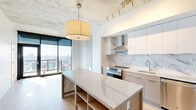 Located at 81 E 14th St in the heart of Kansas City, MO, this contemporary single-floor residence blends industrial and modern design elements to create a sophisticated urban living environment. Exposed concrete ceilings and structural columns provide an authentic industrial character, while light hardwood flooring and crisp white walls keep the aesthetic clean and bright throughout.

The kitchen is a standout feature, outfitted with flat-front cabinetry in both white and warm wood tones, a dramatic marble-veined backsplash, and stainless steel appliances including a range, refrigerator, dishwasher, and a dedicated wine cooler. A generously sized center island with a matching marble-look quartz countertop provides additional prep space and open storage beneath.

The living area is bathed in natural light, courtesy of expansive floor-to-ceiling windows and sliding glass doors that open to a balcony, offering sweeping views of the Kansas City skyline. Exposed concrete columns accent the open living space, reinforcing the unit's modern industrial character.

The bathroom is elegantly appointed with a dual-sink vanity featuring wood and white cabinetry, quartz countertops, large-format tile flooring, and a fully tiled walk-in shower with glass enclosure and multiple shower fixtures, lending a spa-like atmosphere.