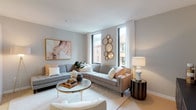 This single-floor residence offers a thoughtfully designed layout with a cohesive contemporary aesthetic defined by neutral tones, light hardwood-style flooring, and an abundance of natural light. The open-concept living area serves as the heart of the home, featuring large windows with city views, sheer drapery, and ample space for comfortable seating arrangements. A glass-top coffee table and curved sectional sofa contribute to the room's refined yet welcoming atmosphere.

The kitchen is efficiently designed with two-toned cabinetry — crisp white upper cabinets paired with dark lower units — white quartz countertops, a tiled backsplash, and stainless steel appliances including a range, microwave, and refrigerator. A dining area adjacent to the kitchen accommodates a bar-height table with seating.

Both bedrooms are well-proportioned, featuring neutral walls, soft carpeting, and generous closet storage with double doors. The primary bathroom includes a sleek dark-cabinetry vanity, wide-format dark tile flooring, and a large mirror. The second bathroom mirrors this aesthetic, offering a glass-enclosed shower, matching cabinetry, and built-in shelving for added storage convenience.