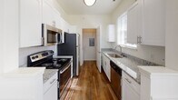 Located at 2004 Calvary Cir in Charlottesville, Virginia, this single-story home presents a well-organized layout with thoughtfully finished interiors throughout. The living area serves as a central gathering space, highlighted by a classic fireplace with a white-painted mantel and tile surround, crown molding, and a ceiling fan overhead. Natural light filters through multiple windows fitted with blinds, casting bright patterns across the plush carpeted floors. An interior pass-through window connects the living area to an adjacent space, enhancing the open feel of the floor plan.

The kitchen is designed for functionality, featuring a galley-style layout with white shaker cabinetry, granite countertops, a stainless steel sink, and a full suite of stainless steel appliances including a refrigerator, range, microwave, and dishwasher. Warm hardwood-style flooring runs underfoot, complementing the clean, bright cabinetry.

The bedrooms are carpeted and receive ample natural light through tall windows with outdoor greenery views. One room includes a built-in granite-topped desk with white cabinetry above, providing a dedicated workspace. The bathrooms feature tub-shower combinations with classic checkered tile detailing and hardwood-style flooring, offering a tidy, practical finish throughout.