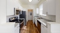 Located at 2004 Calvary Cir in Charlottesville, Virginia, this single-story home presents a well-organized layout with thoughtfully finished interiors throughout. The living area serves as a central gathering space, highlighted by a classic fireplace with a white-painted mantel and tile surround, crown molding, and a ceiling fan overhead. Natural light filters through multiple windows fitted with blinds, casting bright patterns across the plush carpeted floors. An interior pass-through window connects the living area to an adjacent space, enhancing the open feel of the floor plan.

The kitchen is designed for functionality, featuring a galley-style layout with white shaker cabinetry, granite countertops, a stainless steel sink, and a full suite of stainless steel appliances including a refrigerator, range, microwave, and dishwasher. Warm hardwood-style flooring runs underfoot, complementing the clean, bright cabinetry.

The bedrooms are carpeted and receive ample natural light through tall windows with outdoor greenery views. One room includes a built-in granite-topped desk with white cabinetry above, providing a dedicated workspace. The bathrooms feature tub-shower combinations with classic checkered tile detailing and hardwood-style flooring, offering a tidy, practical finish throughout.