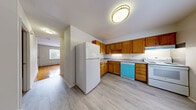 Located at 218 Surrey Dr in Bristol, Connecticut, this multi-floor home offers a practical and comfortable layout spread across three levels, including a basement. The main living area features an open kitchen and living room combination, where warm honey-toned hardwood floors meet light-colored luxury vinyl plank in the kitchen zone. The kitchen is well-appointed with an L-shaped layout, warm oak cabinetry offering generous storage, a full suite of white appliances including a refrigerator, electric range, and dishwasher, alongside a window that brings in natural light. The two bedrooms are bright and inviting, each showcasing polished hardwood floors and large windows with outdoor views of the surrounding neighborhood greenery. Baseboard heating is present throughout, ensuring warmth during Connecticut winters. The two bathrooms are clean and functional — one features classic blue tile wainscoting with a tub surround, while the other is a simpler, light-filled space with vinyl plank flooring. Multiple closets are distributed throughout the home, providing ample storage. The basement level adds flexible additional space, and four staircases connect the floors efficiently. Overall, the home presents a clean, neutral palette throughout.