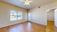 This single-story space is finished with warm-toned hardwood-style flooring that runs consistently throughout every room, creating a cohesive and easy-to-maintain interior. The living area is generously sized, featuring a ceiling fan with integrated lighting, a large window fitted with horizontal blinds that invites natural light, and a glass-panel entry door providing direct outdoor access and additional brightness. A partial wall with a breakfast bar separates the living space from the kitchen, maintaining an open feel while defining each functional zone.

The galley-style kitchen is lined on both sides with light wood cabinetry offering ample upper and lower storage. It is equipped with a white refrigerator, dishwasher, double-basin sink, and an electric range. A central electrical panel is also accessible from within the kitchen.

The bedroom is a comfortable size, featuring a ceiling fan, a window with natural views, and direct access to a spacious walk-in closet outfitted with multi-tiered wire shelving systems along two walls, providing generous organization capacity.

The bathroom includes a wood-toned vanity with overhead cabinetry, a white countertop, toilet, and a full bathtub, all finished with the same consistent hardwood-style flooring found throughout the space.