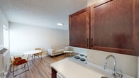 This single-floor unit offers a functional and efficiently designed layout that maximizes every area of the space. The open-concept kitchen and living area serves as the heart of the unit, where rich dark-wood cabinetry with sleek bar-pull hardware contrasts cleanly against white countertops and a white electric coil range with an over-range microwave. A sink and additional cabinetry complete the kitchen, which flows seamlessly into the living and dining area. The living space accommodates a compact dining setup alongside a seating area, all unified by warm light wood-tone laminate flooring that extends throughout the unit. Neutral white walls and a textured ceiling contribute to a clean, understated aesthetic.

The bedroom is a well-sized private retreat featuring a built-in closet with dark wood sliding doors offering ample storage. A stacked washer and dryer unit is conveniently located directly within the bedroom area. The bathroom includes vinyl flooring, white walls, and a shower with a curtain rod. A wall-mounted flat-screen television in the main living area and a gray entry door complete the practical features of this straightforward, move-in-ready space.