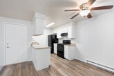 This single-floor residence offers a practical and comfortable layout spread across several well-defined living areas. The living room serves as the central gathering space, featuring plush wall-to-wall carpeting, a tile-surround fireplace with a clean mantle, and a large sliding glass door dressed with vertical blinds that floods the room with natural light and provides outdoor access. A baseboard heating system runs along the perimeter, ensuring efficient warmth throughout. An adjacent hallway connects the living spaces to the private areas of the home, with neutral-toned carpet and flush ceiling lighting guiding the way. The galley-style kitchen is efficiently designed with white shaker cabinetry, light countertops, and wood-look flooring. Black appliances — including a refrigerator, electric range, and dishwasher — provide a bold contrast against the bright cabinetry, while a skylight overhead adds natural illumination. The bedroom features soft carpeting, a sliding-door closet, a baseboard heater, and a window with vertical blinds that casts natural light across the room. The full bathroom is finished with wood-look flooring, a single-sink vanity with white cabinetry and a large mirror, and a combined tub-shower unit. Neutral wall tones and consistent finishes throughout create a cohesive and move-in-ready atmosphere.