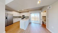 This well-designed three-story residence offers a functional and modern layout spread across three distinct levels. The ground floor houses an attached garage with an automatic opener, providing secure and convenient vehicle storage, along with an entry area that connects to the upper floors via carpeted staircases.

The main living level features a bright, open-concept kitchen and living room finished with light hardwood-style flooring throughout. The kitchen is equipped with stainless steel appliances — including a French door refrigerator, electric range, and built-in microwave — complemented by crisp white shaker cabinetry, a subway tile backsplash, light quartz countertops, and a central island with a sink. Pendant lighting accents the island, while a sliding glass door opens to a private balcony with open views beyond.

The upper floor is dedicated to the generously sized primary bedroom, featuring plush carpet, a ceiling fan, and a trio of windows that invite ample natural light. Two closets provide substantial storage, including a walk-in closet with wire shelving systems. A full bathroom and a dedicated laundry room with wire shelving and a window complete the top level, keeping everyday conveniences within easy reach of the bedroom.