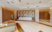 This 1,080 square foot space in Coral Gables, FL, showcases a harmonious blend of modern design and functionality. The single-floor layout is characterized by its open concept, allowing for seamless flow between areas. Upon entry, visitors are greeted by expansive floor-to-ceiling windows that flood the interior with natural light and offer views of the surrounding landscape.

The space features a sophisticated color palette dominated by neutral tones, with warm wood accents providing contrast and depth. A standout element is the custom-built shelving unit, which serves as both a practical storage solution and an artistic display area. The unit's geometric design adds visual interest to the room.

Lighting plays a crucial role in the ambiance, with recessed ceiling lights and subtle LED strips creating a warm, inviting glow. The tray ceiling adds dimension and enhances the sense of space. Luxurious finishes are evident throughout, from the sleek marble-like flooring to the gold inlays that add a touch of elegance.

The seating areas are thoughtfully arranged, with plush, contemporary furniture inviting relaxation and conversation. A striking piece of minimalist artwork serves as a focal point, perfectly complementing the overall aesthetic.

This space successfully combines style and practicality, offering a versatile environment suitable for various purposes, be it a high-end office, a chic reception area, or an upscale residential space.