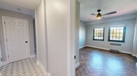 This 2-bedroom, 1-bathroom residence offers a refined living experience defined by consistent design details and quality finishes throughout. Striking herringbone-patterned hardwood floors run through the main living areas and bedrooms, lending a classic yet contemporary character to the space. The entry hallway transitions seamlessly into the living and sleeping areas, with patterned tile flooring adding visual interest near the entryway.

The primary bedroom is a well-proportioned retreat featuring dual windows with dark-framed grilles that invite generous natural light and neighborhood views. A ceiling fan adds comfort, and a convenient closet provides practical storage. The second bedroom also benefits from dual windows and a ceiling fan, with the same warm herringbone flooring tying the rooms together.

The kitchen is efficiently designed with white shaker cabinetry, quartz countertops, a subway tile backsplash, a matte black faucet, and patterned tile flooring that coordinates with the entryway. A window over the sink brings in natural light.

The bathroom is clean and modern, featuring a tub-shower combination enclosed by a sliding glass door with matte black hardware, white tile surround, a frosted window, and the same decorative tile flooring found in the kitchen and hallway. Neutral gray walls and crisp white trim unify the entire residence with a polished, cohesive aesthetic.