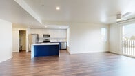 This well-designed 4-bedroom, 2-bathroom residence offers a thoughtful single-floor layout with a clean, contemporary aesthetic throughout. The open-concept kitchen and living area serves as the heart of the home, featuring rich hardwood-style flooring, recessed lighting, and an eye-catching kitchen island with a bold navy blue base and crisp white countertop. The kitchen is equipped with full stainless steel appliances — including a refrigerator, range, microwave, and dishwasher — complemented by two-tone cabinetry with white upper cabinets and navy lower cabinets. Large windows flood the space with natural light, and a sliding glass door opens to a private balcony with outdoor views. The living area is further enhanced by a ceiling fan and generous open space. The four bedrooms feature plush carpeting, windows with blinds for natural light and privacy, and sliding closet doors with built-in hanging rods. The two bathrooms are finished with blue accent flooring, white tub-shower combos, and vanities with white countertops. Multiple hallways connect the layout efficiently, creating a functional and comfortable flow throughout the residence.