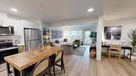 Located in Renton, WA, this two-bedroom, two-bathroom residence at Solera offers a thoughtfully designed single-floor layout with a clean, contemporary aesthetic throughout. Light wood-style flooring flows seamlessly across the open-concept main living area, connecting the kitchen, dining space, and living room into a cohesive, functional zone. The kitchen is well-appointed with stainless steel appliances, two-tone cabinetry featuring white uppers and warm wood-finish lowers, white countertops, and recessed lighting. The open living room is bright and inviting, with large windows and sliding glass door access to a private balcony that brings in generous natural light. Both bedrooms are comfortably scaled, with the primary bedroom offering a spacious layout, and each room includes dedicated closet storage. Three closets total provide ample organization throughout the unit. The two full bathrooms are finished with light wood flooring, white vanities with undermount sinks, and shower-tub combinations. A connecting hallway links the private quarters to the main living area, completing a practical and well-proportioned floor plan suited for everyday living.