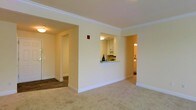 This single-floor residence offers a thoughtfully arranged layout that balances openness with defined living spaces. The main living area is finished with plush wall-to-wall carpeting and features elegant crown molding along the ceiling, lending a refined character to the space. Warm, neutral tones on the walls create a bright and welcoming ambiance throughout.

A distinctive pass-through window connects the kitchen to the living area, promoting an open and airy feel while maintaining a sense of separation between the spaces. The kitchen is equipped with white cabinetry and built-in appliances, offering a clean and functional design. Adjacent to the kitchen, a hallway with hardwood-style flooring leads to additional rooms, providing a natural transition between areas.

The floor plan, as visible in the dollhouse view, reveals a practical and efficient use of space, with clearly defined zones for living, cooking, and sleeping. Each room benefits from the home's consistent neutral palette and ample interior lighting. A bathroom accessible from the main corridor adds convenience to the layout. Overall, the space presents a comfortable and cohesive environment, well-suited for everyday living.