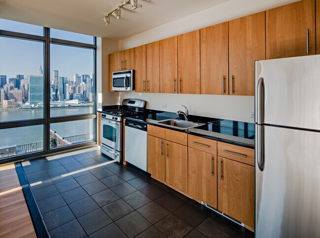 Cocina del Paquete Clásico III con electrodomésticos de acero inoxidable, gabinetes de arce, encimeras de granito negro y pisos de baldosas. - Avalon Riverview