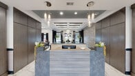 Located at 317 Stallion Circle West in Toms River, NJ, this single-story amenity center presents a sophisticated, contemporary design throughout its various functional spaces. The entrance foyer sets an refined tone with large-format marble-look tile flooring, an arched transom window above double glass doors, a coffered ceiling with a statement chandelier, and flanking wall sconces that establish an inviting first impression.

The main corridor continues the marble-look tile and features warm wood-paneled accent walls alongside textured decorative panels, creating a polished transition between spaces. A spacious event hall offers coffered ceilings with tray details finished in deep teal, complemented by ring pendant fixtures and an abundance of natural light from multiple windows framed by floor-length drapery. A dedicated billiards lounge features a full-size pool table beneath a modern cluster pendant light, with an adjacent dining area.

A cozy lounge nook provides upholstered seating, patterned wallcoverings, and herringbone-accented flooring. A conference room includes a round table, whiteboard, and an outdoor view. The fitness center is accessible through glass-paned double doors and features marble-look tile flooring and decorative mosaic tile accents. Throughout, patterned carpeting, navy trim details, and curated décor unify the space with a consistently modern aesthetic.