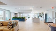 Located at 160 S Ventura Ave in Ventura, California, this single-floor community space combines coastal-inspired design with modern functionality. The open-plan layout is anchored by large-format light-toned tile flooring that flows seamlessly throughout, creating a cohesive and airy atmosphere.

The fully equipped kitchen is a standout feature, showcasing light gray flat-panel cabinetry, a generous waterfall-edge island with bar seating, stainless steel appliances including a double wall oven and French door refrigerator, and a vibrant geometric diamond-pattern tile accent wall. Decorative pendant lights hang above the island, adding warmth and visual interest.

The lounge area offers generous sectional seating accented with coastal-toned throw pillows in teal, orange, and sand. Built-in shelving provides display space for curated décor, while a live-edge wood coffee table adds an organic touch. Indoor planter boxes filled with lush greenery serve as natural dividers between zones, contributing to the fresh, resort-like ambiance.

A dedicated dining nook features a striking live-edge wood communal table surrounded by modern chairs and a wraparound upholstered banquette. Ocean-inspired framed artwork lines the walls above, illuminated by sculptural cage pendant lights. Abundant natural light pours in through expansive windows and glass doors that open to an outdoor patio, reinforcing the space's bright, welcoming character.