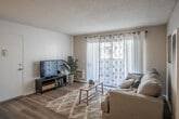 This single-floor residence offers a thoughtfully arranged layout that connects the living, dining, and kitchen areas in an open, functional flow. The living room is a welcoming space, featuring light-toned laminate flooring, a textured ceiling, and large sliding glass doors dressed with decorative sheer curtains that allow generous natural light to fill the room. A wall-mounted HVAC unit and a built-in vent provide climate control throughout the space.

Adjacent to the living area, the dining space is anchored by a ceiling fan with a light fixture and comfortably accommodates a full dining set. The kitchen is efficiently designed with white cabinetry extending to the ceiling for ample storage, speckled countertops, a gas range, dishwasher, double-basin sink, and a window that brings in additional natural light. The flooring continues seamlessly from the living and dining areas.

The bedroom is a quiet retreat with soft carpeting, vertical blinds over a well-sized window, and a textured ceiling. The bathroom maintains the home's cohesive aesthetic with speckled countertops, a framed mirror, and clean white fixtures, offering a tidy and functional space.