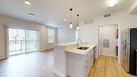 Located on Longs Peak Street in Brighton, Colorado, this one-bedroom, one-bathroom residence offers a thoughtfully designed open-concept layout with modern finishes throughout. Light wood-tone flooring flows through the main living areas, anchoring the bright and airy atmosphere created by large windows and recessed lighting.

The kitchen serves as a central hub of the space, featuring a peninsula island with a stainless steel sink, light quartz countertops, crisp white cabinetry with brushed hardware, a subway tile backsplash, and stainless steel appliances including a range and over-the-range microwave. Stylish pendant lights hang above the island, adding a refined touch. The kitchen transitions seamlessly into the living room, which is highlighted by a sliding glass door that provides direct outdoor access and fills the room with natural light.

The bedroom is a comfortable retreat with plush carpet, a ceiling fan, and an abundance of natural light from a bank of oversized windows fitted with blinds. An adjacent walk-in closet offers dedicated shelving and rod storage. The full bathroom features gray cabinetry, a wide vanity with a framed mirror, and a soaking tub. A dedicated laundry area and hallway complete the functional layout of this well-appointed Brighton residence.