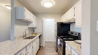 This single-floor, 1-bedroom, 1-bathroom residence offers a thoughtfully designed layout that maximizes both functionality and comfort. The galley-style kitchen is a standout feature, equipped with stainless steel appliances including an electric range, dishwasher, and refrigerator. White cabinetry lines both sides of the kitchen, complemented by granite-style countertops and a stainless steel sink, all set atop durable wood-look flooring. The open living room is bright and inviting, featuring crown molding, a ceiling fan, rich wood-look flooring, a tiled fireplace, and sliding glass doors that open to a balcony with outdoor views. The spacious bedroom is finished with plush carpeting, a ceiling fan, and a window that allows natural light to fill the room. The full bathroom includes a granite-topped vanity with white cabinetry, a tub-shower combination, and wood-look flooring. Additional conveniences include a dedicated laundry area with an in-unit washer hookup, a closet for extra storage, and a connecting hallway that ties the layout together seamlessly. The unit's soft neutral tones throughout create a calm and cohesive aesthetic.