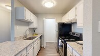 This single-floor, 1-bedroom, 1-bathroom residence offers a thoughtfully designed layout that maximizes both functionality and comfort. The galley-style kitchen is a standout feature, equipped with stainless steel appliances including an electric range, dishwasher, and refrigerator. White cabinetry lines both sides of the kitchen, complemented by granite-style countertops and a stainless steel sink, all set atop durable wood-look flooring. The open living room is bright and inviting, featuring crown molding, a ceiling fan, rich wood-look flooring, a tiled fireplace, and sliding glass doors that open to a balcony with outdoor views. The spacious bedroom is finished with plush carpeting, a ceiling fan, and a window that allows natural light to fill the room. The full bathroom includes a granite-topped vanity with white cabinetry, a tub-shower combination, and wood-look flooring. Additional conveniences include a dedicated laundry area with an in-unit washer hookup, a closet for extra storage, and a connecting hallway that ties the layout together seamlessly. The unit's soft neutral tones throughout create a calm and cohesive aesthetic.