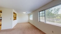 Located within the Figure Eight community on Regina Drive in East Windsor, Connecticut, this single-floor unit offers a functional and straightforward layout designed for everyday comfort. The living area is generously proportioned, featuring neutral wall-to-wall carpeting and cream-colored walls that create a clean, bright atmosphere. Multiple windows fitted with blinds allow natural light to filter in throughout the space, providing views of the surrounding greenery.

A pass-through opening connects the living area to the kitchen, enhancing the sense of openness between the two spaces. The kitchen is efficiently arranged in an L-shaped configuration, offering laminate countertops with wood-trim detailing, white cabinetry, a double-basin sink, a dishwasher, and tile flooring — providing ample workspace and storage.

The bedroom features soft carpeting, a window with outdoor views, and textured ceilings consistent throughout the unit. The bathroom includes a tub-shower combination enclosed by sliding glass doors with chrome framing, complemented by tile flooring. A staircase visible in the floor plan model suggests access to a lower level or entry area. Overall, the unit maintains a neutral, move-in-ready aesthetic throughout.