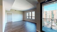 Located at 399 Main Ave in Norwalk, Connecticut, this single-floor residence offers a thoughtfully designed layout with a clean, contemporary aesthetic. The open living area is anchored by rich hardwood flooring and benefits from large windows that frame views of the surrounding cityscape and greenery, filling the space with natural light. Track lighting overhead adds a modern touch and enhances the room's versatility. A pass-through window connects the living area to the kitchen, creating an open and connected feel. The kitchen is well-equipped, featuring white shaker-style cabinetry, stainless steel appliances including a gas range and refrigerator, a dishwasher, and light wood flooring that complements the crisp countertops and clean lines throughout. The bedrooms offer plush carpeting for comfort, with windows that bring in additional natural light and views of the urban surroundings. Each bedroom provides ample space and includes closet access. The bathroom is finished with classic white tile accented by a decorative checkered border, complete with a full soaking tub and shower combination. A dedicated in-unit laundry closet houses a full-sized washer and dryer, adding everyday convenience. Overall, the space presents a functional and comfortable urban living environment.