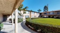 This ground-floor unit is situated within a two-story residential complex that showcases classic stucco construction with a warm beige exterior finish. The buildings are arranged to frame a generous central courtyard, which serves as the visual and social heart of the property. The shared outdoor space features a well-kept lawn, neatly trimmed hedges forming curved borders along concrete walkways, and mature trees including palms that contribute to a distinctly Southern California character.

The unit's exterior includes sliding windows that allow for natural light and ventilation, complemented by wall-mounted air conditioning units for climate control. A textured stucco facade runs the length of the building's exterior walls, giving the property a cohesive and durable appearance. The side yards are maintained with grass and landscaped shrubbery, adding greenery throughout the grounds.

Residents benefit from covered walkways and exterior staircases that connect the buildings, creating a community-oriented layout. The overall ambiance is calm and well-organized, with thoughtful landscaping and open sky views enhancing the sense of space throughout the communal areas.
