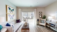 This single-floor residence offers a thoughtfully designed layout that balances comfort and functionality across its multiple rooms. The living area serves as the heart of the home, featuring wood-look plank flooring, warm neutral walls, and a sliding glass door framed by decorative curtains that opens onto a private balcony — allowing natural light to fill the space and providing outdoor views.

Adjacent to the living area, the dining space accommodates a full-sized table and chairs, accented by light grey walls and wood-look flooring that flows consistently throughout the common areas.

The kitchen is equipped with stainless steel appliances, including an electric range, over-the-range microwave, and refrigerator. Medium-toned cabinetry pairs with granite-style countertops and a light tile backsplash, creating a clean, modern aesthetic.

The bedrooms feature plush carpeting, ample natural light from large windows with blinds and decorative curtains, and ceiling fans. At least one bedroom includes an attached bathroom. A secondary full bathroom features wood-look flooring, a single-sink vanity with dark cabinetry, and a walk-in shower.

A dedicated laundry area with a full-sized washer and dryer completes the practical offerings of this well-rounded residence.