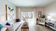 This single-floor residence offers a thoughtfully designed layout that balances comfort and functionality across its multiple rooms. The living area serves as the heart of the home, featuring wood-look plank flooring, warm neutral walls, and a sliding glass door framed by decorative curtains that opens onto a private balcony — allowing natural light to fill the space and providing outdoor views.

Adjacent to the living area, the dining space accommodates a full-sized table and chairs, accented by light grey walls and wood-look flooring that flows consistently throughout the common areas.

The kitchen is equipped with stainless steel appliances, including an electric range, over-the-range microwave, and refrigerator. Medium-toned cabinetry pairs with granite-style countertops and a light tile backsplash, creating a clean, modern aesthetic.

The bedrooms feature plush carpeting, ample natural light from large windows with blinds and decorative curtains, and ceiling fans. At least one bedroom includes an attached bathroom. A secondary full bathroom features wood-look flooring, a single-sink vanity with dark cabinetry, and a walk-in shower.

A dedicated laundry area with a full-sized washer and dryer completes the practical offerings of this well-rounded residence.
