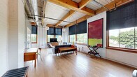 Located at 340 Rutgers St in Rochester's vibrant 14607 neighborhood, this one-bedroom, two-bathroom unit showcases a striking industrial-chic aesthetic with thoughtful modern updates throughout. The open layout is defined by soaring ceilings with exposed wooden beams, visible ductwork, and painted white brick walls that lend a distinctive loft-style character.

The living room is bathed in natural light from oversized wood-framed windows fitted with roller shades, offering leafy neighborhood views. Light hardwood flooring flows throughout, unifying each space.

The well-appointed kitchen features dark cabinetry, stainless steel appliances, a farmhouse-style sink with a professional-grade faucet, white subway tile backsplash, and stone countertops. A large concrete-topped island with reclaimed wood legs doubles as a dining area, illuminated by pendant lighting beneath the exposed beam ceiling.

The generously sized primary bedroom accommodates a four-poster canopy bed and includes ample closet space, exposed industrial ceiling elements, and an antler-style chandelier that adds a unique design touch.

The bathrooms are clean and modern, featuring wood-framed vanities, stone countertops, and white tile finishes that echo the unit's overall aesthetic. An in-unit laundry area adds everyday convenience, completing this distinctive and well-designed urban residence.