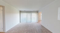 This single-floor residence offers a thoughtfully laid-out interior designed for comfortable everyday living. The living area is generously proportioned, featuring warm beige carpeting and a large sliding glass door dressed with vertical blinds that allow natural light to filter through while offering outdoor access. The open layout connects seamlessly to adjacent spaces, creating an easy flow throughout the home.

The kitchen is functional and well-appointed, featuring warm oak cabinetry that extends to the ceiling with crown molding detail, dark laminate countertops, and durable hardwood-style flooring. It is equipped with a full suite of appliances including a refrigerator, electric range, dishwasher, and microwave, along with a dedicated pantry cabinet for additional storage. A decorative column adds an architectural accent to the space.

The bedrooms are carpeted and bright, with neutral wall tones and ample square footage. One bedroom features an arched window offering pleasant outdoor views, adding a distinctive architectural touch. The bathroom includes a walk-in shower enclosed in a sleek glass-framed door and finished with elegant marble-style tiling, complemented by clean, neutral fixtures. Overall, the space presents a clean, move-in-ready environment with a consistent neutral palette throughout.