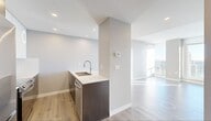 The View is a thoughtfully designed 2-bedroom, 2-bathroom residence that blends modern aesthetics with functional living. Light hardwood flooring flows throughout the unit, complemented by neutral-toned walls that create a bright, cohesive ambiance. The kitchen is a standout feature, equipped with dark espresso cabinetry contrasted by crisp white upper cabinets and quartz countertops. A double stainless steel sink, tile backsplash, and stainless steel appliances—including a French door refrigerator and electric range—complete this well-appointed space. A built-in countertop ledge adjacent to the kitchen offers a convenient workspace or dining area. Both bedrooms are generously sized relative to the overall footprint, bathed in natural light from large floor-to-ceiling windows that frame sweeping city skyline views. The primary bedroom includes a sliding-door closet with built-in shelving. The two bathrooms feature elegant marble-look tile flooring and dark vanity cabinetry with white quartz countertops; one bathroom includes a glass-enclosed shower, while the other offers a soaking tub and shower combination. Recessed lighting and roller shades throughout the unit add a polished, modern finish to this light-filled urban residence.