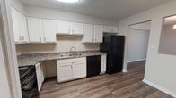 This single-floor residence at Regal Park offers a well-designed layout that balances functionality and comfort throughout its living spaces. Rich wood-look plank flooring runs through the main living and dining areas, providing a warm and cohesive aesthetic, while plush carpet in the bedrooms adds a comfortable, cozy feel.

The kitchen is outfitted with ample white shaker-style cabinetry, granite-look countertops, and a full suite of black appliances, including a refrigerator, range with over-the-range microwave, and dishwasher. A double-basin sink is positioned beneath the upper cabinetry, and a bifold-door closet nearby provides convenient pantry or storage space.

The dining area connects seamlessly to the kitchen and is accented by an elegant chandelier overhead. The living area features a distinctive blue accent wall that adds a pop of color and visual interest to the space. A separate room, likely a bedroom, features plush carpeting, a ceiling fan with light fixture, and a window that brings in natural light.

Additional bedrooms offer generous proportions with carpeted floors and closet access. The bathroom includes a tub-shower combination with white surround, wood vanity with granite-look countertop, and wood-look flooring. Throughout the unit, textured ceilings and clean white trim complete the well-maintained interior.