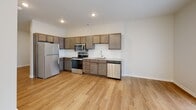 This well-appointed single-floor unit offers a thoughtfully designed open-concept layout that seamlessly connects the kitchen and living areas, creating a bright and functional living environment. Light-toned hardwood-style flooring runs throughout the space, lending warmth and visual continuity from room to room.

The kitchen is a standout feature, outfitted with rich, medium-toned wood cabinetry providing generous storage, granite-style countertops, and a full suite of stainless steel appliances including a refrigerator, range, over-the-range microwave, and dishwasher. Recessed lighting illuminates the space efficiently, highlighting the clean white walls that give the kitchen an airy, modern feel.

The living area is spacious and filled with natural light from a grid-style window, creating a welcoming atmosphere. A private entry door adds convenience and a sense of independence to the space.

A dedicated laundry area includes a full-size stacked washer and dryer unit alongside built-in wire shelving, offering practical storage and in-unit laundry convenience. The bathroom is clean and simply finished with hardwood-style flooring and crisp white walls. The overall design aesthetic throughout the unit is modern and minimalist, with consistent finishes that create a cohesive and move-in-ready living space.