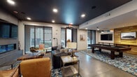 Located in Memphis, TN, this single-floor club room delivers a well-appointed communal space designed for both socializing and productive gatherings. The space is unified by polished concrete floors and dark, dramatic ceilings fitted with recessed lighting, creating a contemporary industrial ambiance throughout.

The lounge area anchors the space with a bold, geometric-patterned area rug layered beneath leather seating, including tan armchairs and a dark sofa. A standout feature wall showcases a linear fireplace flanked by a built-in wood storage niche and a wall-mounted television, lending warmth and visual interest. Large sliding glass doors admit abundant natural light and provide views of the surrounding streetscape.

Adjacent to the lounge, the games area features a full-size pool table set against a warm wood-paneled accent wall adorned with framed photography. Multi-colored pendant lights and a mounted flat-screen television complete this entertainment zone. A decorative metal chain-link partition elegantly separates zones while maintaining an open sightline.

The conference room offers a striking live-edge wood table surrounded by multicolored chairs, illuminated by circular pendant fixtures. A wood-slat ceiling, geometric wallcovering, vibrant artwork, and a wet bar with refrigeration make it well-suited for meetings or private events.