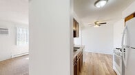 Located at 620 Gorman St in Shakopee, MN, this single-floor 1-bedroom, 1-bathroom unit offers a practical and well-organized layout. The kitchen is a galley-style space featuring rich wood cabinetry, granite-look countertops, a gas range, refrigerator, and a sink with additional storage. Light wood-look flooring runs through the kitchen and connecting areas, giving these spaces a clean, modern feel. A ceiling fan overhead adds airflow and light to the open dining area adjacent to the kitchen. The bedroom is a comfortable, well-proportioned room finished with plush carpeting, a ceiling fan with light fixture, and a large window with vertical blinds that allows natural light to fill the space. A built-in closet provides convenient storage. The hallway connects the main rooms efficiently and features wood-toned doors that add a warm contrast to the bright white walls. The bathroom is finished with full white square tile surrounding the bathtub and shower, complemented by built-in shelving and classic white fixtures, creating a clean and functional space. Throughout the unit, white walls and neutral tones create a bright, cohesive ambiance well-suited to comfortable everyday living.