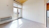 Located at 7141 Woodbine Ave in Sacramento, CA, this thoughtfully designed two-floor unit offers a clean, modern aesthetic across its intimate layout. The main floor hosts the primary living areas, including an open living space bathed in natural light through large French doors that lead to an outdoor balcony, offering pleasant views of surrounding greenery. The soaring ceiling on this level is finished with warm natural wood planking and exposed industrial ductwork, lending a contemporary loft-like character to the space. Polished concrete-style flooring runs throughout, adding to the modern, minimalist feel. The compact kitchen is efficiently designed with light oak cabinetry, a built-in oven, cooktop, stainless steel refrigerator, and a single-basin sink with a sleek faucet — all complemented by clean white countertops and ample upper storage. The bathroom is well-appointed with full-height tile surrounding a soaking tub and handheld shower fixture in brushed gold, a wall-mounted sink, an LED-lit vanity mirror, and matching oak overhead cabinetry. The upper floor provides additional flexible space. Throughout the unit, the palette of white walls, natural wood tones, and concrete flooring creates a cohesive, bright, and contemporary living environment.