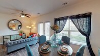This single-story, one-bedroom, one-bathroom residence offers a thoughtfully designed open-concept layout that maximizes its comfortable footprint. The living area features wood-style flooring, a ceiling fan, and abundant natural light streaming through large windows and a glass-panel exterior door that opens to an outdoor space. Sheer dark curtain panels add a stylish contrast to the bright interior.

The dining area flows seamlessly from the living space, accommodating a round dining table with easy access to the kitchen. The kitchen is a standout feature, boasting dark espresso cabinetry, granite-style countertops, stainless steel appliances, and a peninsula island with pendant lighting and bar seating. A dedicated pantry closet adds generous storage.

The bedroom is a serene retreat with plush carpeting, multiple windows, and a ceiling fan. The full bathroom includes a granite-topped dark vanity, wood-style flooring, and a tub-shower combination. An in-unit washer area with shelving provides added convenience. The overall ambiance is warm, cohesive, and move-in ready.