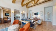Located in Travelers Rest, SC, this thoughtfully designed single-floor community clubhouse offers a variety of inviting spaces suited for both relaxation and socializing. The centerpiece is a dramatic great room with soaring vaulted ceilings accented by striking exposed wood beam trusses, warm hardwood-style flooring, and a curated mix of comfortable seating in rich blue and orange tones that creates a vibrant yet welcoming atmosphere.

Adjacent dining areas are bathed in natural light through floor-to-ceiling windows and glass doors, offering sweeping views of the outdoor pool area and surrounding community. Round bistro tables with woven leather chairs provide casual seating perfect for gathering.

A dedicated kitchenette features a bold striped accent wall, wall-mounted TV, ample cabinetry, and a generous white quartz island with bar seating — ideal for hosting events. The game room offers entertaining options including a pool table and shuffleboard, with natural light filtering through transom windows.

A refined coworking lounge rounds out the space, showcasing built-in shelving, individual workstations, pendant lighting, a statement chandelier, and a tiled fireplace with a stacked wood display — blending productivity with warmth and elegance throughout.
