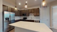 Located at 891 Ingleside Ave in Columbus, Ohio, this well-appointed single-floor residence offers a thoughtfully designed layout with contemporary finishes throughout. The open-concept kitchen is a standout feature, showcasing rich dark wood cabinetry, crisp white quartz countertops, a tile mosaic backsplash, and a full suite of stainless steel appliances including a refrigerator with ice maker, electric range, microwave, and dishwasher. A generously sized center island with pendant lighting provides additional prep space and casual seating, while wood-look plank flooring grounds the space with warmth and durability. The living area extends naturally from the kitchen, bathed in natural light from large windows with transom panels that frame views of lush greenery outside. Bedrooms are finished with plush carpeting and feature oversized windows that continue the theme of abundant natural light. Each bathroom is outfitted with dark wood vanities, white quartz countertops, framed mirrors, and wood-look flooring. The bathrooms connect to spacious walk-in closets with built-in shelving systems, offering excellent storage. A dedicated laundry area houses a full-size top-loading washer and dryer, adding everyday convenience to this polished and functional home.