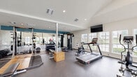 Located at 626 Shug Jordan Pkwy in Auburn, Alabama, this fitness center offers a thoughtfully designed exercise room that provides a comprehensive workout environment. The space features soaring vaulted and high ceilings that lend an open, airy feel, complemented by an abundance of natural light streaming through large windows along multiple walls. French doors at one end open to an outdoor view, further enhancing the bright and welcoming atmosphere.

The exercise room is equipped with a diverse range of fitness equipment to support varied workout routines. Cardio options include treadmills, an elliptical trainer, and a stationary cycle, while strength training is well-supported by a multi-station cable machine, a squat rack with barbells, a dedicated free weights area with a dumbbell rack, and a flat bench. Stability balls, medicine balls, and a yoga mat round out the functional fitness offerings.

Durable rubber flooring covers the workout area, providing both safety and comfort during exercise. Wall-mounted flat-screen televisions are positioned throughout the space for entertainment. A mirrored wall expands the sense of space visually, and a built-in water fountain ensures convenient hydration. The clean, neutral color palette with a teal accent wall creates a motivating and energetic atmosphere, making this fitness center a well-appointed facility for residents.